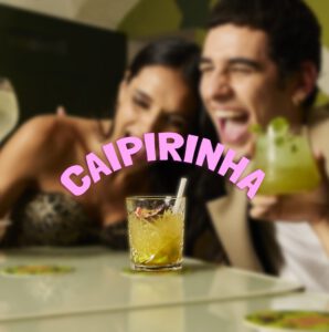 Due ospiti ridono al tavolo con una caipirinha in mano
